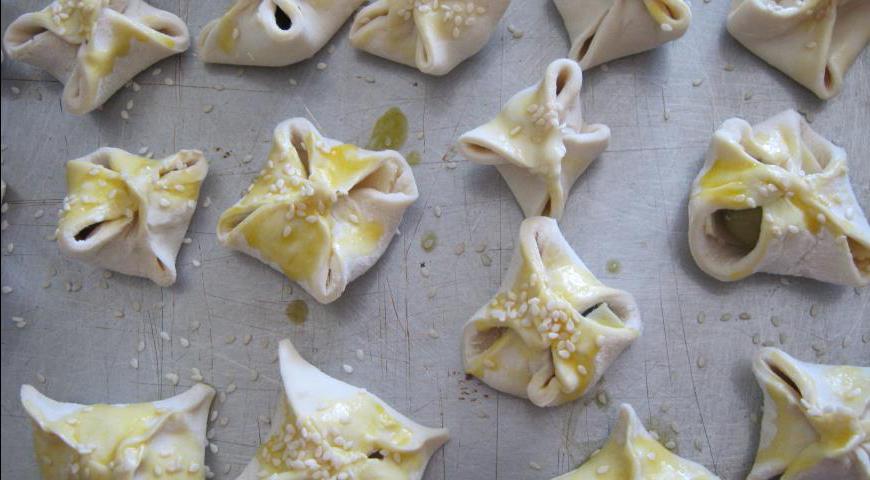 Полученные заготовки смазываем взбитым желтком и посыпаем кунжутом. Выпекаем в предварительно разогретой духовке при температуре 200°C до красивого золотистого цвета.