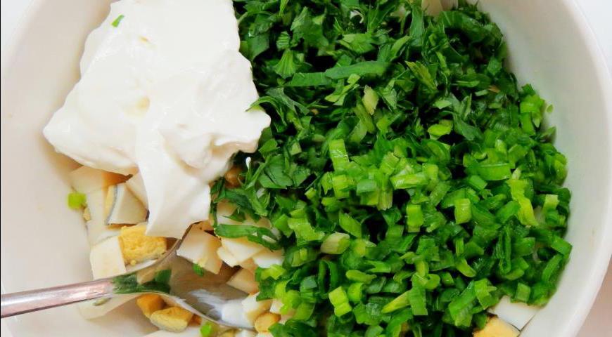 Тем временем готовим начинку. Вареные яйца нарезаем мелкими кубиками, зелень петрушки и зеленый лук измельчаем. Смешиваем все компоненты в миске, добавляем сметану, солим и слегка перчим по вкусу.
