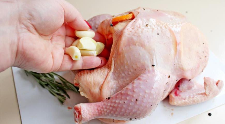 За полчаса до начала приготовления достаньте курицу из холодильника. Осторожно отделите кожу от мяса, особенно на грудке и спинке, стараясь её не повредить. Под кожу вложите кружочки апельсина. Во внутрь курицы положите зубчики чеснока, лимон, оставшийся апельсин и палочку корицы.