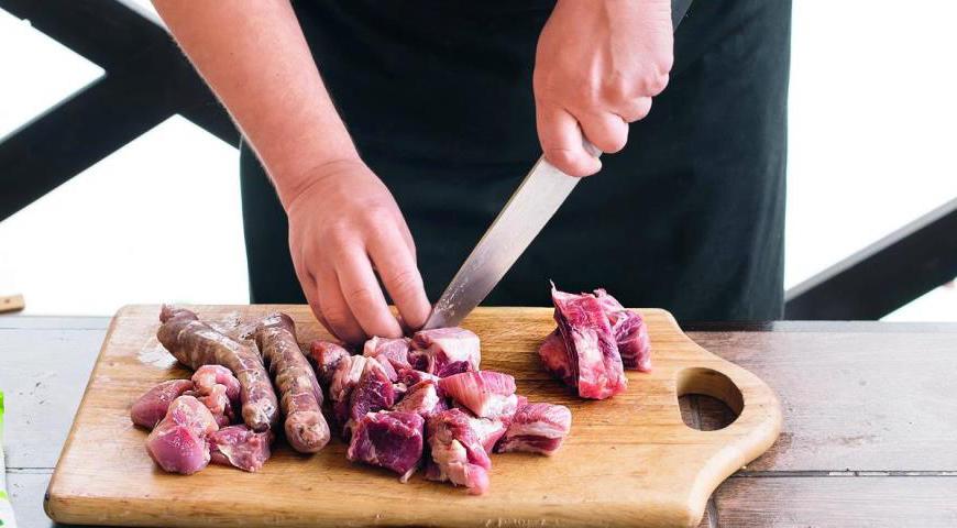 Очистите и измельчите чеснок. Разрежьте куриные окорочка пополам в суставе. Колбаски проткните зубочисткой, чтобы они не лопнули во время жарки. Свинину нарежьте кубиками размером около 3 см, а ребрышки разделите на порционные куски. Зеленую фасоль нарежьте на 2–3 части.