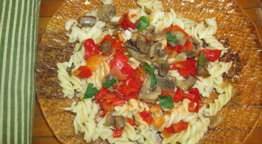 Добавьте отваренную пасту в сковороду с овощами и грибами. Перемешайте, прогрейте несколько минут, чтобы паста впитала ароматы начинки. Подавайте горячей, посыпав рубленой свежей зеленью.