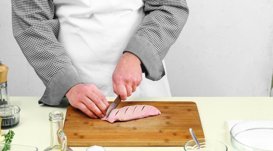 Сделайте крестообразные надрезы на коже грудок, не затрагивая мясо. Поместите их в глубокую миску, посыпьте перцем и смажьте оливковым маслом.