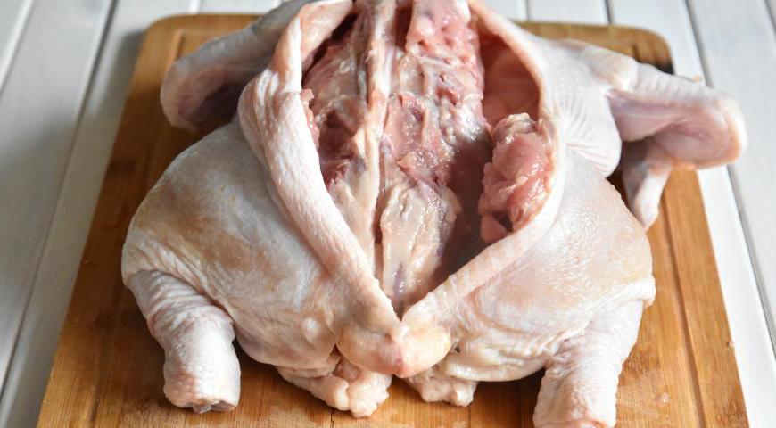 Тщательно промойте тушку курицы и обсушите её бумажными полотенцами. Разрежьте вдоль позвоночника, аккуратно удалите хребет, стараясь не повредить кожу. Оставьте кости в крыльях и ножках. Соедините разрезанные части кожи зубочистками, затем переверните курицу грудкой вверх для дальнейшей подготовки.