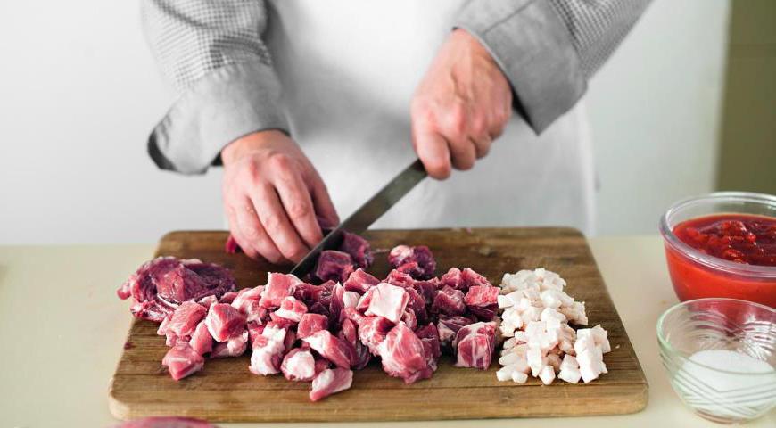 Нарежьте мясо кубиками размером около 2 см. Сало нарежьте мелкими кубиками (4–5 мм). В кастрюлю с толстым дном положите сало, поставьте на маленький огонь и вытопите.
