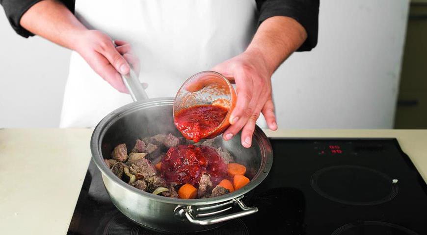 Выньте мясо из бульона, дав стечь жидкости, и положите его к луку с чесноком. Готовьте на среднем огне в течение 3 минут. Добавьте томатный соус, доведите до кипения и тушите на небольшом огне 5 минут.