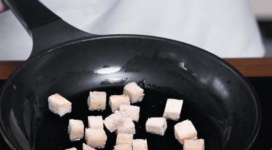 С хлеба срежьте корки, мякиш нарежьте кубиками со стороной 1 см. В другой сковородке поменьше разогрейте 3,5–4,5 ст. л. масла, положите целые очищенные зубчики чеснока и обжаривайте на маленьком огне, помешивая, 6 мин. Выньте чеснок, поместите его в ступку. В сковороду с маслом положите кубики хлеба, обжаривайте до коричневато-золотистой корочки, помешивая, 3 мин. Выньте хлеб, положите к чесноку, сковороду отставьте.