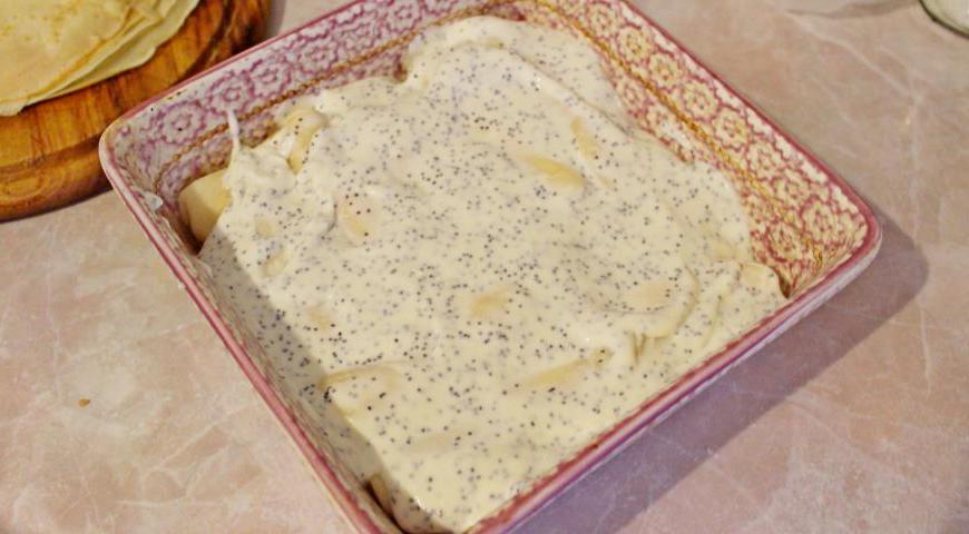 Для заливки смешиваем сметану с маком и 2 столовыми ложками сахара. Хорошо перемешиваем, чтобы сахар полностью растворился. Поливаем этой смесью блины, равномерно распределяя по всей поверхности. Отправляем форму в предварительно разогретую духовку до температуры 180°C и запекаем 12–15 минут, до образования золотистой корочки сверху.