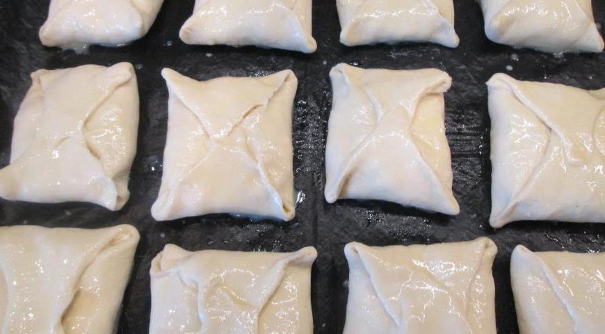Смешайте яичный желток с молоком. Каждый квадрат с начинкой аккуратно сложите конвертом, защипните края и смажьте сверху желтковой смесью. Уложите изделия на противень, накройте полотенцем и дайте настояться около 20 минут.