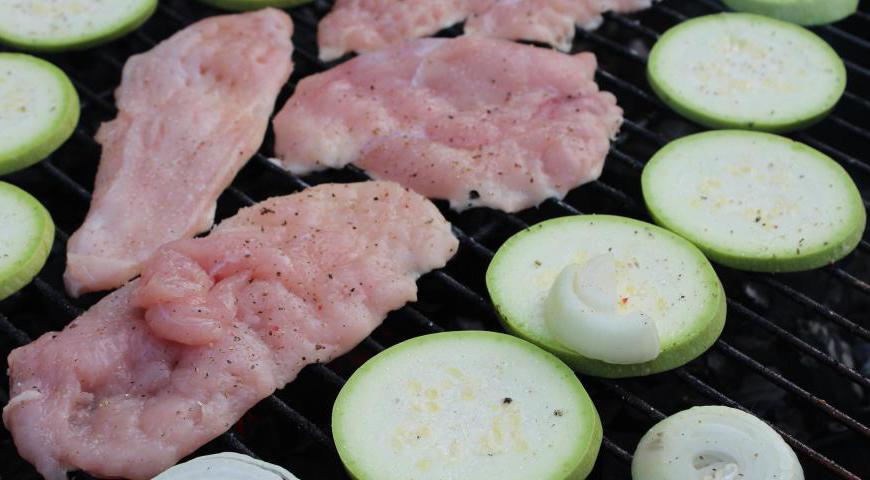 Куриную грудку слегка отбиваем, чтобы мясо лучше прожарилось, солим и перчим с обеих сторон. На гриль-решетку выкладываем филе, а рядом — нарезанные кружочками кабачок и лук. Если кто-то из гостей не любит жареный лук, его можно добавить сырым в саму лепешку.