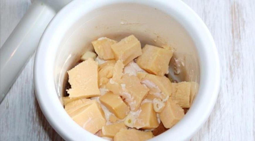 Переложите немного остывшее куриное филе с луком в чашу блендера. Добавьте порезанный сыр и измельченный чеснок. Перемешайте до получения однородной массы.