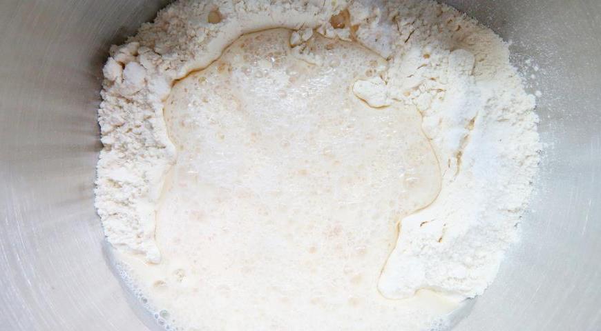 В глубокой миске смешайте просеянную муку с сухими дрожжами и сахаром. Добавьте воду, в которую предварительно растворите соль. Если вы планируете печь оладьи через час-полтора, используйте теплую воду, а если хотите оставить тесто на ночь — возьмите холодную. Хорошо перемешайте тесто до однородности. Не переживайте, если сразу оно получится немного комковатым — за время брожения оно станет более гладким.