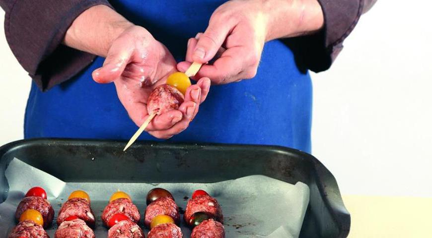 Разогрейте духовку до 185 °C. Насадите фрикадельки и помидоры черри на подготовленные шпажки, чередуя их. Уложите шашлычки на противень, застеленный пергаментной бумагой. Запекайте около 18 минут до готовности фрикаделек. Подавайте блюдо горячим.