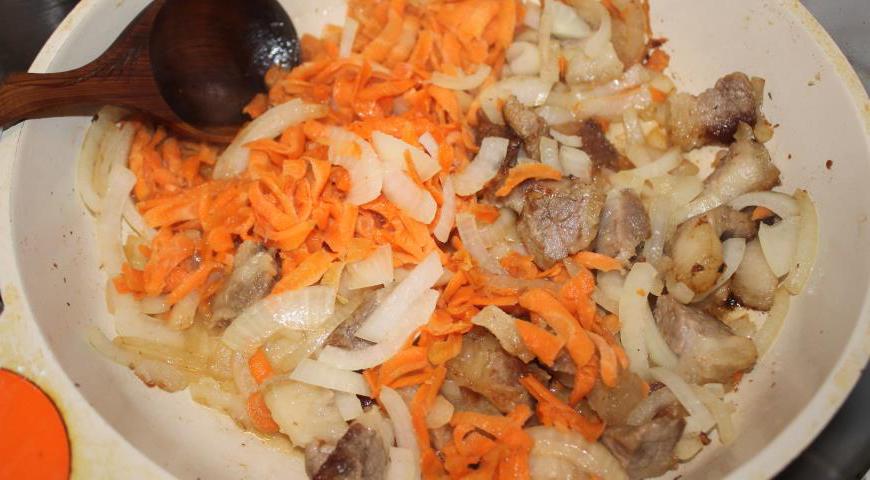 Очистите лук и нарежьте его произвольными кусочками. Морковь почистите и натрите на крупной тёрке. Добавьте овощи в сковороду к мясу и немного протушите.