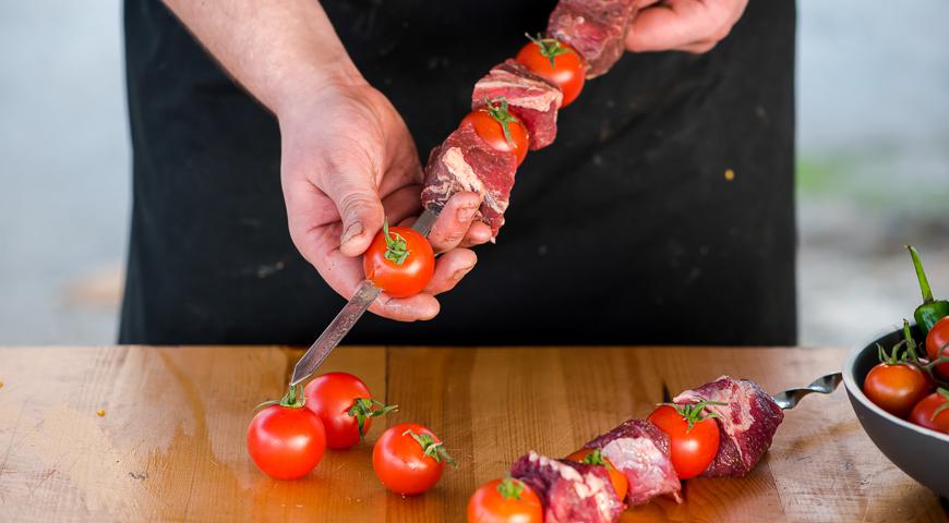 Нанизывайте мясо на шампуры, чередуя с помидорами черри. Обжаривайте на раскаленной решетке мангала примерно 35 минут, периодически переворачивая шашлыки для равномерной прожарки.