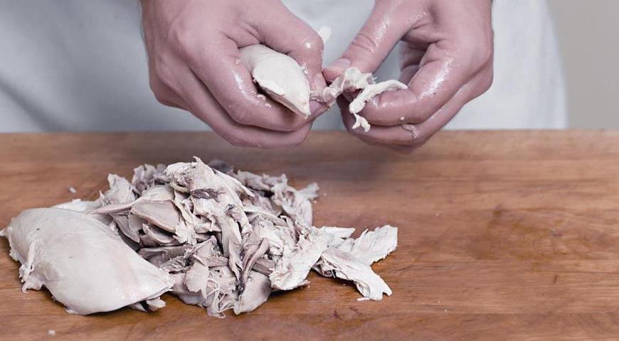 Выньте курицу из бульона, процедите жидкость. Дайте курице немного остыть, снимите мясо с костей и разделите на небольшие кусочки.