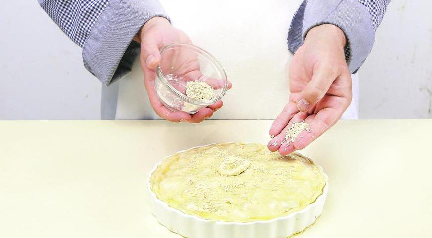 Смажьте тесто оливковым маслом, щедро посыпьте кунжутом. Дайте пирогу расстояться в теплом месте 18–22 минуты. Затем выпекайте примерно 42 минуты. Подавайте горячим или остывшим.