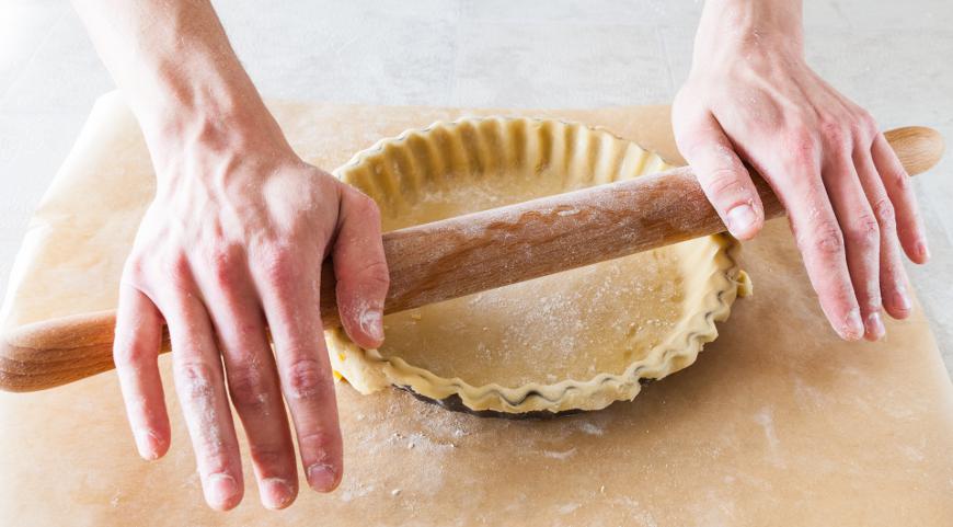 Разогрейте духовку до 180 °C. Раскатайте охлаждённое тесто скалкой и перенесите его в форму диаметром около 30 см или прямоугольную форму аналогичного объёма. Уберите лишнее тесто по краям, равномерно распределите по дну и бортам формы.