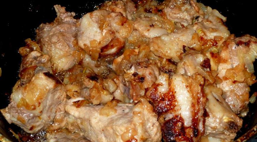 Добавьте к луку подготовленные свиные ребрышки. Обжаривайте мясо несколько минут, чтобы оно слегка зарумянилось и сохранило сочность внутри.