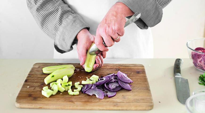Очистите огурец и лук. Лук нарежьте тонкими полукольцами. Разрежьте огурец вдоль, удалите семена с помощью острой ложки, а затем нарежьте мякоть поперек на кусочки толщиной около 1 см. Добавьте огурцы и лук в заправку.