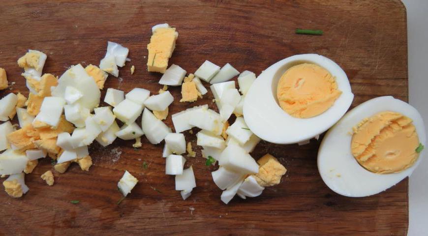 Очистите вареные яйца и нарежьте их небольшими кубиками.