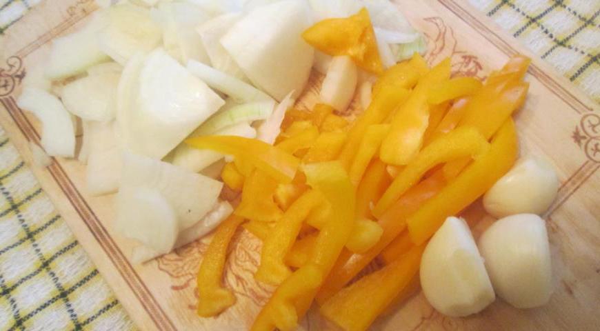 Картофель тщательно промываем, не очищая кожуру. Наливаем на сковороду немного растительного масла и хорошо разогреваем. Выкладываем картофель и обжариваем под крышкой около 15 минут, периодически помешивая. За это время нарезаем лук полукольцами, болгарский перец полосками, а чеснок измельчаем через пресс.