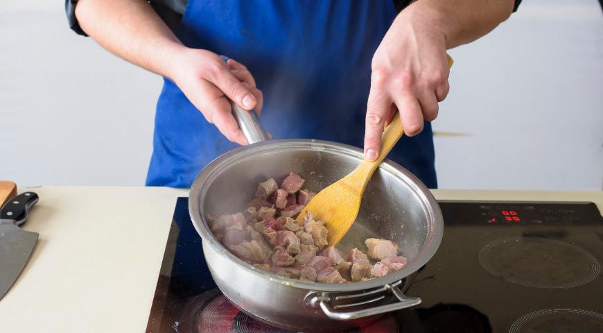 Овощи нарежьте кубиками размером примерно 1 см. Говядину разрежьте крупными кусками. В огнеупорной кастрюле с высокими бортиками нагрейте растительное масло и обжарьте мясо до золотистой корочки.