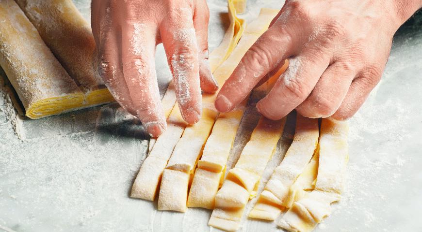 Острым ножом или ножом для пиццы нарежьте тесто на полоски нужной ширины. Чтобы они получились ровными, слегка присыпьте тесто мукой, сверните в рулон и нарежьте. После разверните полоски и дайте им немного подсохнуть на воздухе. Храните готовую пасту в герметичном контейнере до 3–4 дней.