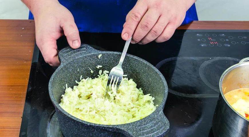 Пока тушится рыба, приготовьте рис. Очистите и мелко нарежьте лук и чеснок. В небольшой кастрюле разогрейте масло и обжарьте лук и чеснок до золотистого цвета. Добавьте рис и перемешайте.