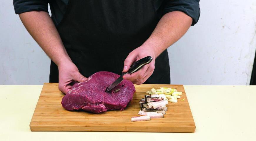 С помощью острого ножа аккуратно сделайте надрезы в мякоти под углом 90°, чтобы внутри образовалась полость. В каждую из них вставьте кусочки сала и чеснока, используя зубочистки для удобства. После этого тщательно намажьте мясо горчицей, чтобы придать ему пикантности. Заверните в пищевую пленку и оставьте в холодильнике минимум на сутки.