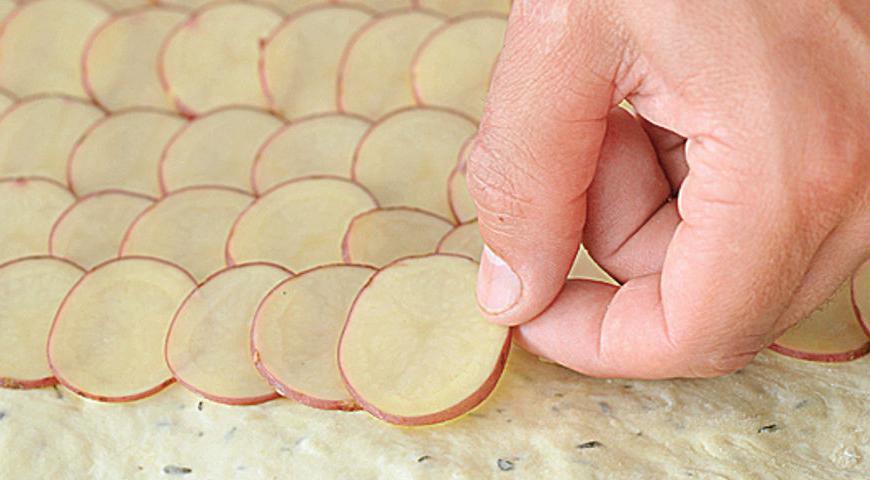 Тщательно вымойте молодой картофель щеткой и нарежьте тонкими кружками. Распределите кружочки по тесту ровными рядами, внахлест. Удалите чеснок из масла, полейте картофель маслом с розмарином и приправьте солью и перцем.