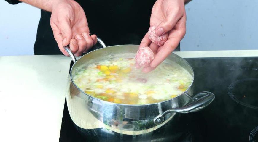 Увеличьте огонь под кастрюлей с супом и доведите его до кипения. Добавьте фрикадельки, лавровый лист, рубленые помидоры, зелень, посолите и варите 18 минут при слабом кипении.