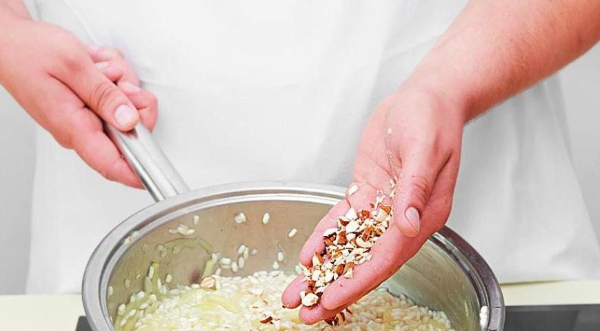 Добавьте обжаренный лук с яблоками к рису, начните понемногу вливать бульон, постоянно помешивая. Готовьте примерно 12–16 минут до полуготовности риса. В конце добавьте последнюю порцию бульона, посолите и перемешайте.