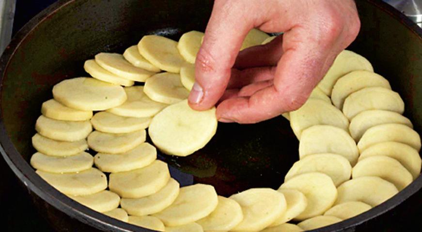 Выложите первый слой картофеля в масло, укладывая кружочки внахлест. Поставьте сковороду на минимальный огонь и продолжайте укладывать картофель быстро и аккуратно, чтобы не повредить форму.