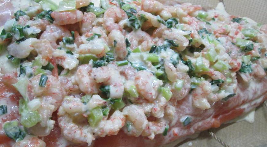 Выложите на противень пергамент, положите на него кусочки кулинарной нити на расстоянии друг от друга. На них поместите одну половину рыбы без надрезов, сверху равномерно распределите начинку и посыпьте приправой.