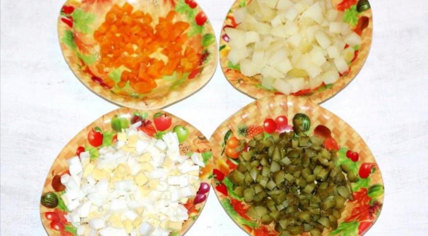 Начнём с подготовки основных компонентов. Картофель и морковь отвариваем в кожуре в слегка подсоленной воде, яйца — вкрутую. После остужаем их, очищаем и нарезаем одинаковыми кубиками. Маринованные огурчики также нарезаем кубиками. Перекладываем всё в большую миску.