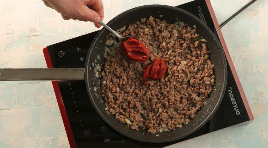 Добавьте томатную пасту, хорошо перемешайте, чтобы она равномерно распределилась. Влейте горячую воду, приправьте специями и тушите 7–8 минут. Макароны откиньте на дуршлаг, затем смешайте их с фаршем и подавайте, посыпав тертым сыром и свежей петрушкой.