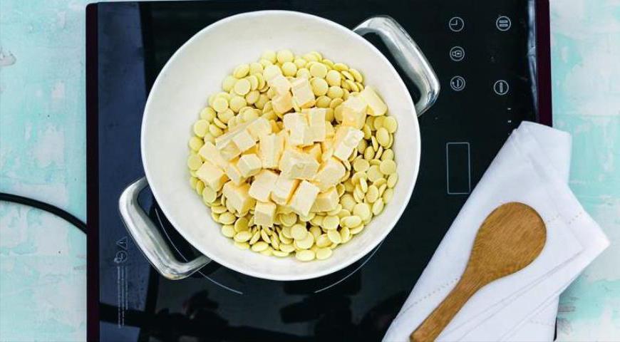 Нарежьте белый шоколад мелкими кусочками и поместите его в глубокую миску. Добавьте сливочное масло, порезанное кубиками, и растопите их на водяной бане, постоянно помешивая до получения однородной массы.