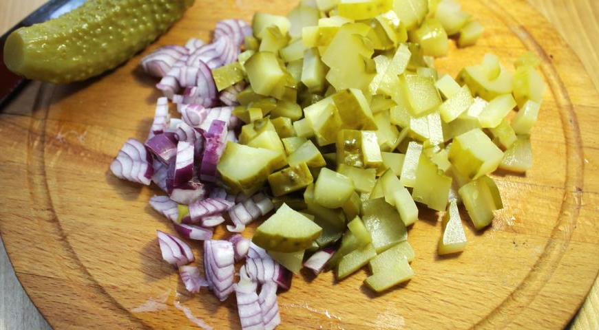 Маринованные огурцы обсушите бумажным полотенцем и нарежьте кубиками. Одну луковицу очистите и мелко порубите. Один огурец нарежьте тонкими ломтиками для последующего украшения блюда.
