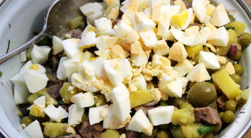 В глубокой миске объедините нарезанные кубики картофеля, языка, огурцов, куриных яиц, добавьте каперсы, оливки и зелёный горошек. Заправьте всё приготовленным соусом и аккуратно перемешайте. Выложите салат через кулинарное кольцо на сервировочные тарелки. Украсьте ломтиками огурца, половинками перепелиных яиц и веточками зелёного лука. Ваш праздничный Оливье готов!