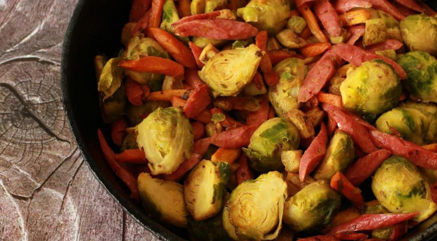 Очередность обжарки играет важную роль в создании вкуса. Разогрейте сковороду на среднем огне. Налейте немного растительного масла и сначала обжарьте морковь до легкого золотистого цвета. Затем добавьте кабачки и продолжайте жарить до появления румяной корочки. После этого отправьте в сковороду брюссельскую капусту, а в последнюю очередь — колбаски.