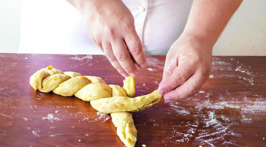 Заплетите жгуты в аккуратную косу, переложите на противень, застеленный пергаментом, и оставьте для второго подъема в теплом месте на 40–50 минут.