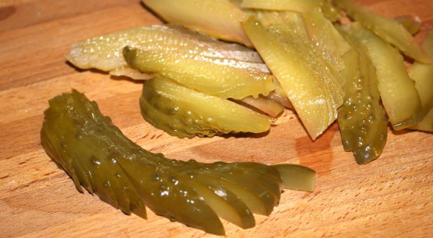 Маринованные огурцы разрежьте вдоль пополам, затем каждую половинку нарежьте тонкими ломтиками. Это придаст салату хрустящую текстуру и яркий кисло-солёный вкус.