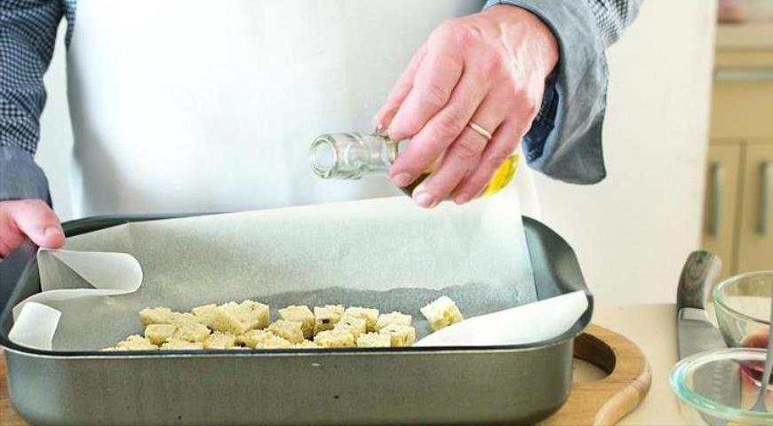 Срежьте с хлеба корки, мякиш нарежьте кубиками размером 1,5 см. Выложите на противень, застеленный пергаментом, сбрызните оливковым маслом и поставьте в духовку, разогретую до 175 °C. Запекайте около 15 минут до золотистого цвета, периодически перемешивая.