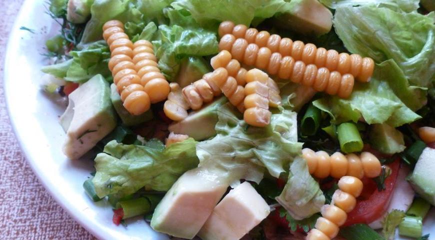 На общую тарелку выложите кукурузу, кубики авокадо и кусочки малосольной красной рыбы. Полейте приготовленной заправкой и сразу же подавайте к столу.