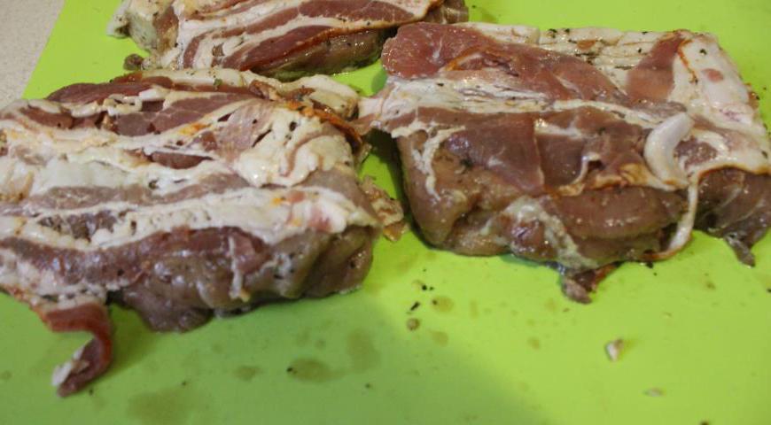 Оберните каждый кусок мяса слайсами бекона, стараясь плотно покрыть поверхность для получения хрустящей корочки.