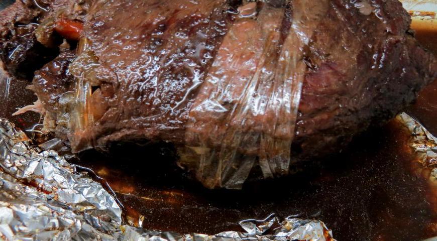 Аккуратно сверните мясо в рулет, зафиксируйте кулинарной нитью или полосками рукава. Обжарьте рулет в нагретом оливковом масле со всех сторон. Влейте 200 мл вина, дождитесь испарения спирта, добавьте стакан бульона. Закройте фольгой и отправьте в духовку при 180°C на 1,5 часа. Периодически поливайте рулет и переворачивайте его.