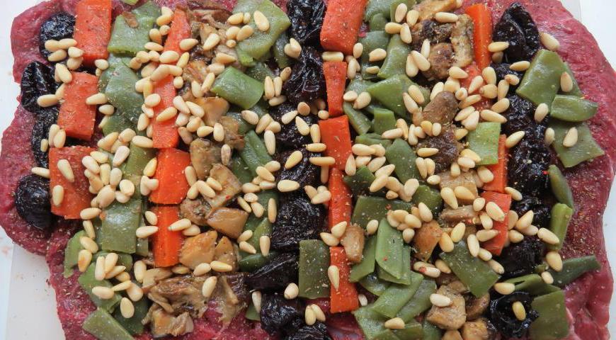 Посолите и поперчите мясо, равномерно распределите начинку: фасоль, чернослив, морковь и грибы. Сверху посыпьте кедровыми орешками.