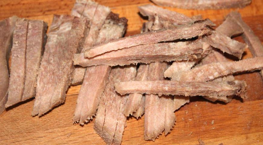 Охлажденный отварной язык тонко нарежьте полосками одинаковой толщины, чтобы он равномерно распределился в салате.