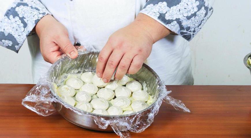 Выберите круглую форму или коробку диаметром 22–24 см. Внутреннюю поверхность застелите пищевой пленкой так, чтобы ее края свободно свисали. Немного смажьте дно кремом, затем аккуратно уложите первый слой безе, стараясь заполнить форму ровно.