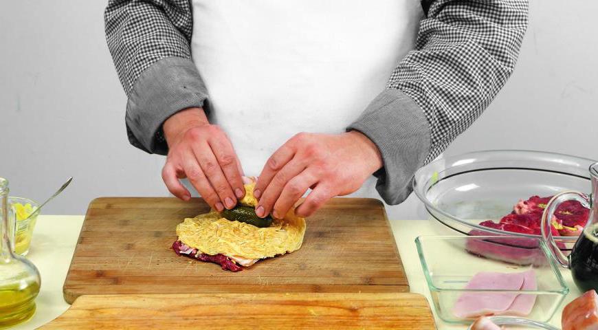 На каждый пласт мяса уложите два кусочка бекона, один ломтик ветчины и готовый омлет. В центр каждого положите по маринованному огурчику.